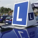 Niebieskie samochody z literą "L" na dachu, symbolizujące naukę jazdy i zasady egzaminu na prawo jazdy.