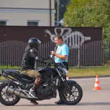 Egzamin kat A na placu manewrowym. Motocyklista w kasku i ochraniaczach rozmawia z instruktorem.