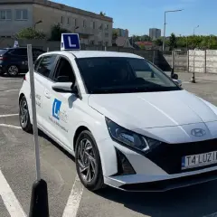 Biały samochód nauki jazdy z literą "L" na dachu, gotowy do egzaminu. Zgoda rodziców na prawo jazdy to pierwszy krok do wolności.