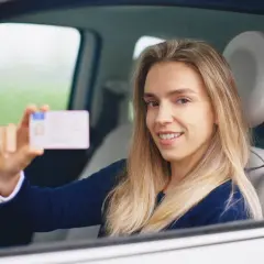 Uśmiechnięta kobieta w samochodzie pokazuje prawo jazdy. Czy na zdjęciu do prawa jazdy muszą być widoczne uszy?
