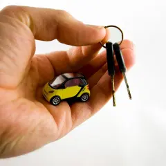 Dłoń trzyma miniaturowy żółty samochód i dwa kluczyki. Zastanawiasz się, ile trwa dorobienie klucza do samochodu?