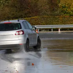 Srebrny samochód na mokrym torze, ćwiczący bezpieczne **jazdy doszkalające dla osób z prawem jazdy**.