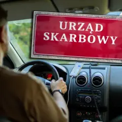 Kierowca w samochodzie widzi tablicę "Urząd Skarbowy", zastanawiając się, ile podatku od zakupu auta zapłaci.
