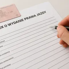 Dłoń z długopisem wypełnia wniosek o wydanie prawa jazdy. Obok leży nowe prawo jazdy.