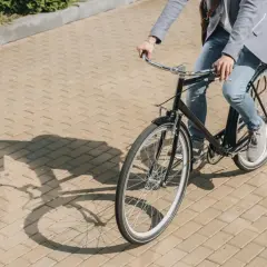 Mężczyzna w marynarce i jeansach jedzie rowerem po chodniku. Czy bez karty rowerowej można jeździć po chodniku?