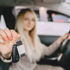 Kobieta w samochodzie pokazuje kluczyki, symbolizując moment, kiedy można zacząć robić prawo jazdy.