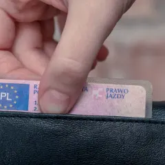 Dłoń wkłada do czarnego portfela polskie prawo jazdy. Widoczny jest numer blankietu prawa jazdy.
