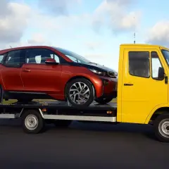 Żółta laweta przewozi czerwony samochód. Zastanawiasz się, ile kosztuje prawo jazdy na lawetę?