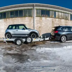 Mini Cooper na lawecie, obok BMW X5. Pokazano, jak zabezpieczyć auto na lawecie, używając pasów.