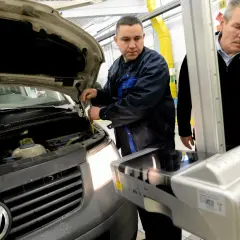 Mechanik sprawdza samochód z otwartą maską, obok stoi urządzenie do ustawiania świateł.
