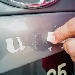 Dłoń usuwa resztki starej naklejki z samochodu, pokazując, jak odkleić naklejkę z samochodu bez śladu.