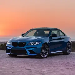 Niebieskie BMW M2 z pakietem M na plaży o zachodzie słońca. To jest m pakiet, który nadaje autu sportowy wygląd i osiągi.