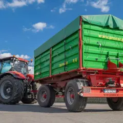 Czerwony traktor z zieloną przyczepą rolniczą. Zastanawiasz się, jak zarejestrować przyczepę rolniczą bez dokumentów? Sprawdź na www.pronar.pl.