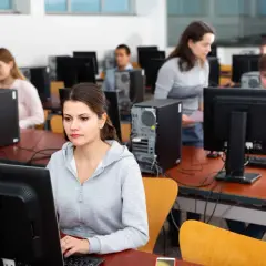 Uczniowie w sali komputerowej ćwiczą, jak zdać teorię na prawko. Skupieni przed monitorami, przygotowują się do egzaminu.