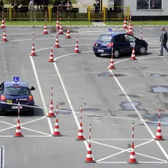Plac manewrowy kat B. Dwa samochody z literą L na dachu i pachołki wyznaczają trasę egzaminu na prawo jazdy.