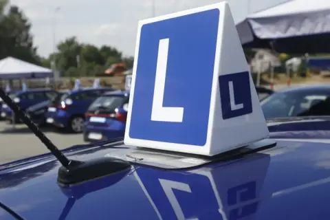 Niebieskie samochody z literą "L" na dachu, symbolizujące naukę jazdy i zasady egzaminu na prawo jazdy.