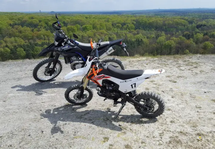 Dwa motocykle crossowe na tle lasu. Czy crossem można jeździć po ulicy? Te maszyny są stworzone do terenu.