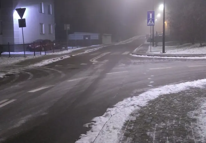 Skrzyżowanie dróg w nocy, z mgłą, śniegiem i znakami drogowymi.