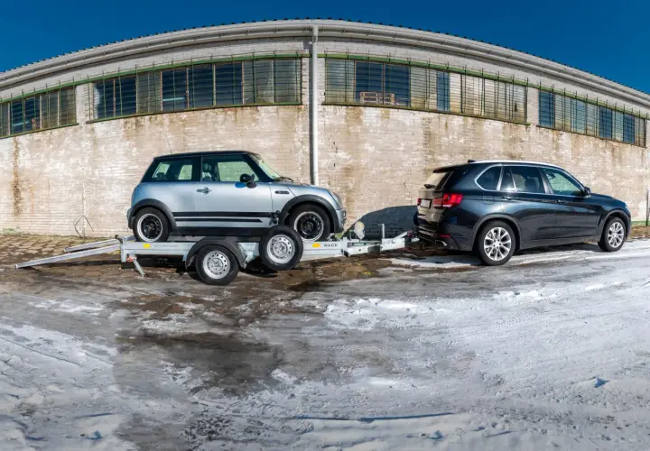 Mini Cooper na lawecie, obok BMW X5. Pokazano, jak zabezpieczyć auto na lawecie, używając pasów.