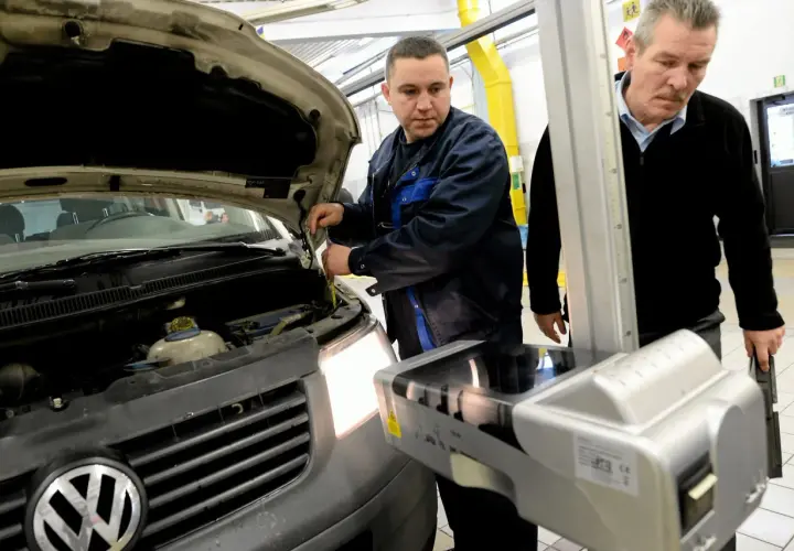 Mechanik sprawdza samochód z otwartą maską, obok stoi urządzenie do ustawiania świateł.