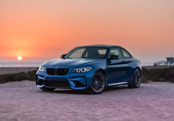 Niebieskie BMW M2 z pakietem M na plaży o zachodzie słońca. To jest m pakiet, który nadaje autu sportowy wygląd i osiągi.