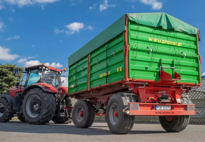 Czerwony traktor z zieloną przyczepą rolniczą. Zastanawiasz się, jak zarejestrować przyczepę rolniczą bez dokumentów? Sprawdź na www.pronar.pl.