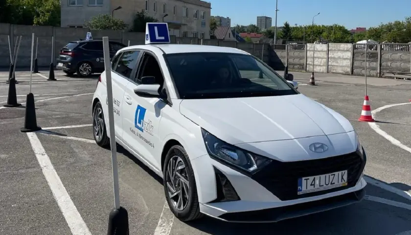 Biały samochód nauki jazdy z literą "L" na dachu, gotowy do egzaminu. Zgoda rodziców na prawo jazdy to pierwszy krok do wolności.