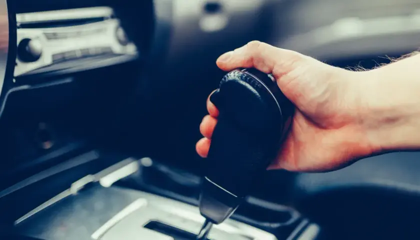 Dłoń trzymająca dźwignię zmiany biegów w samochodzie. Pytanie: czy mając prawo jazdy na automat można jeździć manualem?