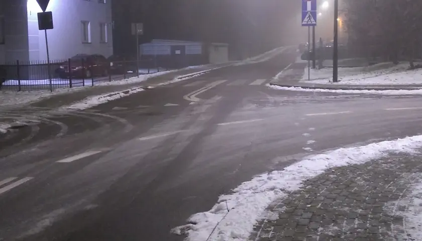 Skrzyżowanie dróg w nocy, z mgłą, śniegiem i znakami drogowymi.