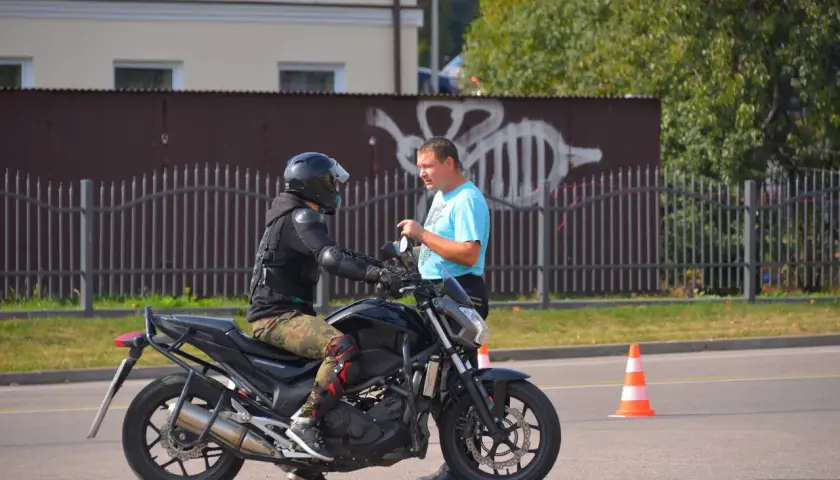 Egzamin kat A na placu manewrowym. Motocyklista w kasku i ochraniaczach rozmawia z instruktorem.