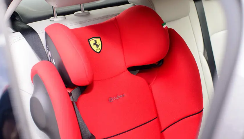 Czerwony fotelik samochodowy Cybex z logo Ferrari, zamontowany za pomocą pasa bezpieczeństwa. Instrukcja jak zamontować fotelik samochodowy.