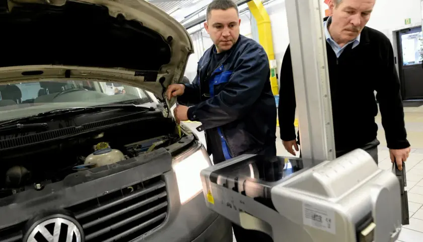 Mechanik sprawdza samochód z otwartą maską, obok stoi urządzenie do ustawiania świateł.