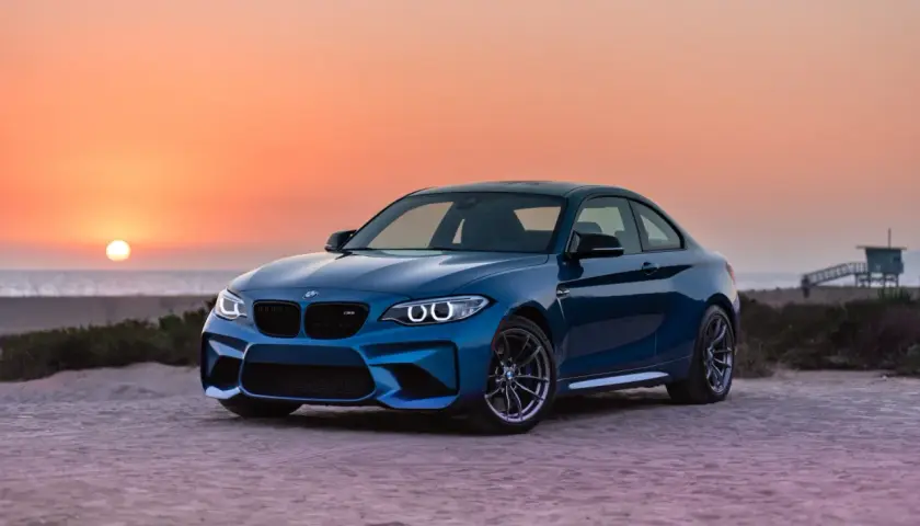 Niebieskie BMW M2 z pakietem M na plaży o zachodzie słońca. To jest m pakiet, który nadaje autu sportowy wygląd i osiągi.