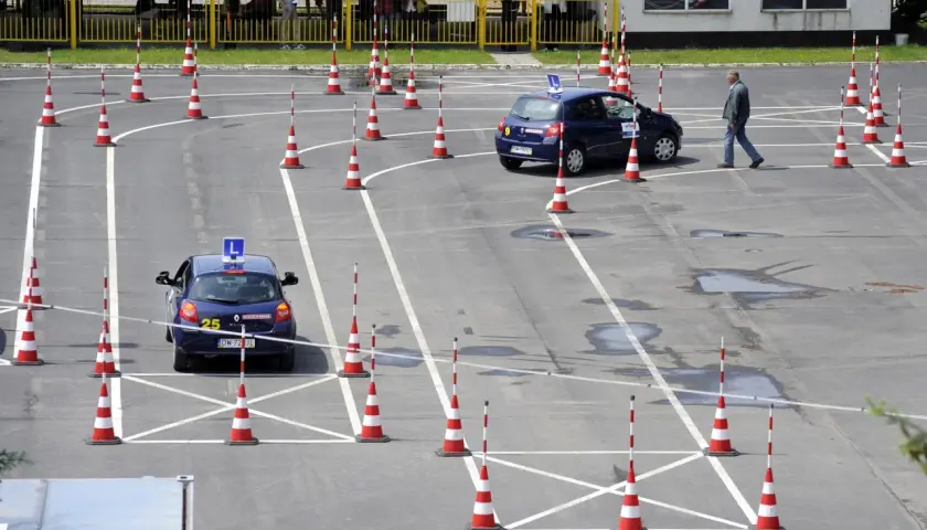 Plac manewrowy kat B. Dwa samochody z literą L na dachu i pachołki wyznaczają trasę egzaminu na prawo jazdy.