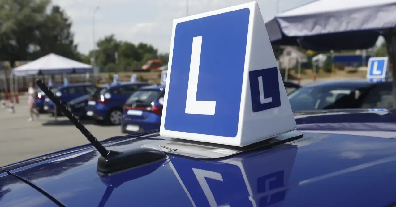 Niebieskie samochody z literą "L" na dachu, symbolizujące naukę jazdy i zasady egzaminu na prawo jazdy.