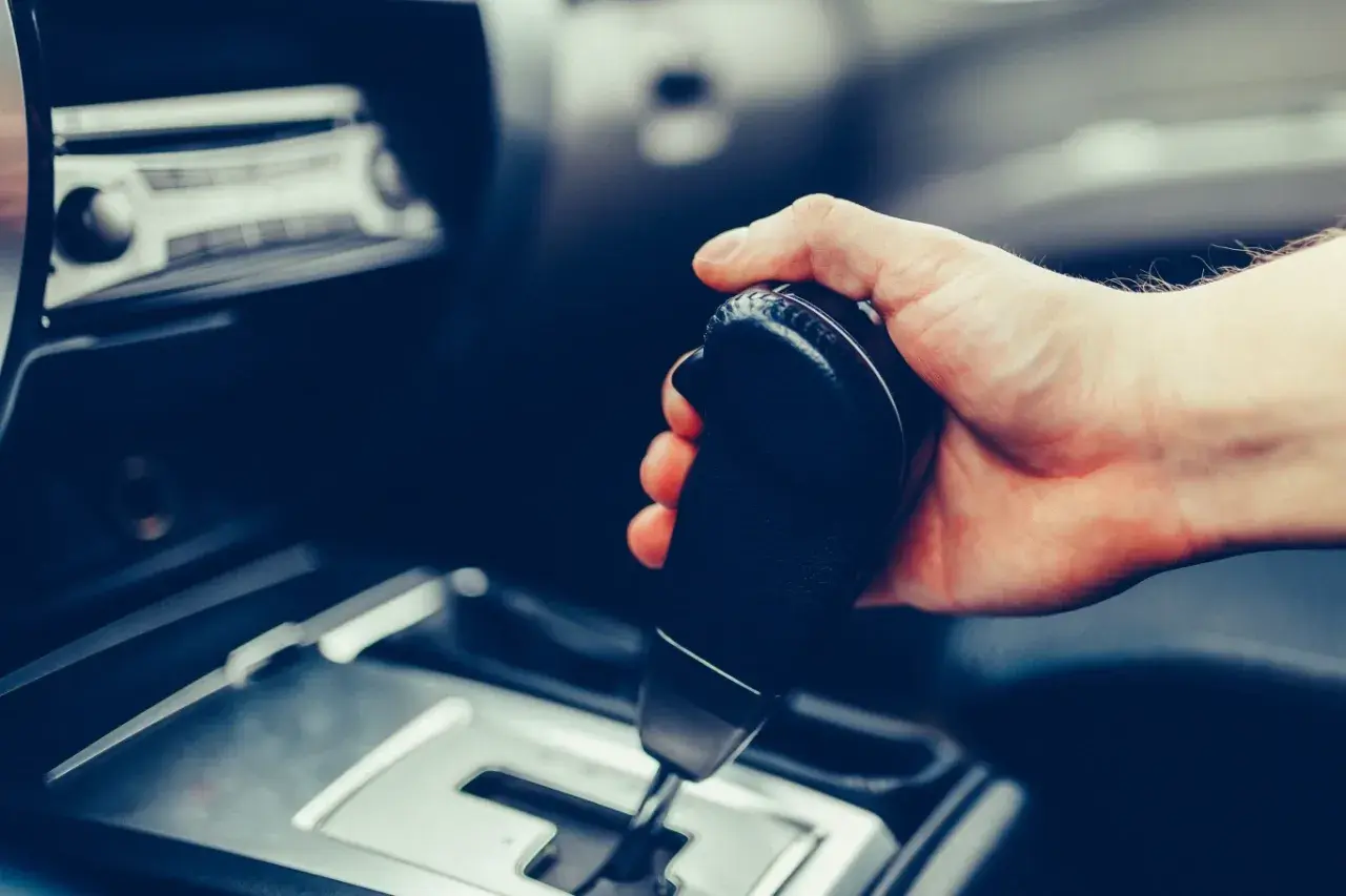 Dłoń trzymająca dźwignię zmiany biegów w samochodzie. Pytanie: czy mając prawo jazdy na automat można jeździć manualem?