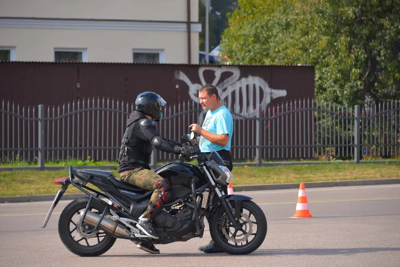 Egzamin kat A na placu manewrowym. Motocyklista w kasku i ochraniaczach rozmawia z instruktorem.