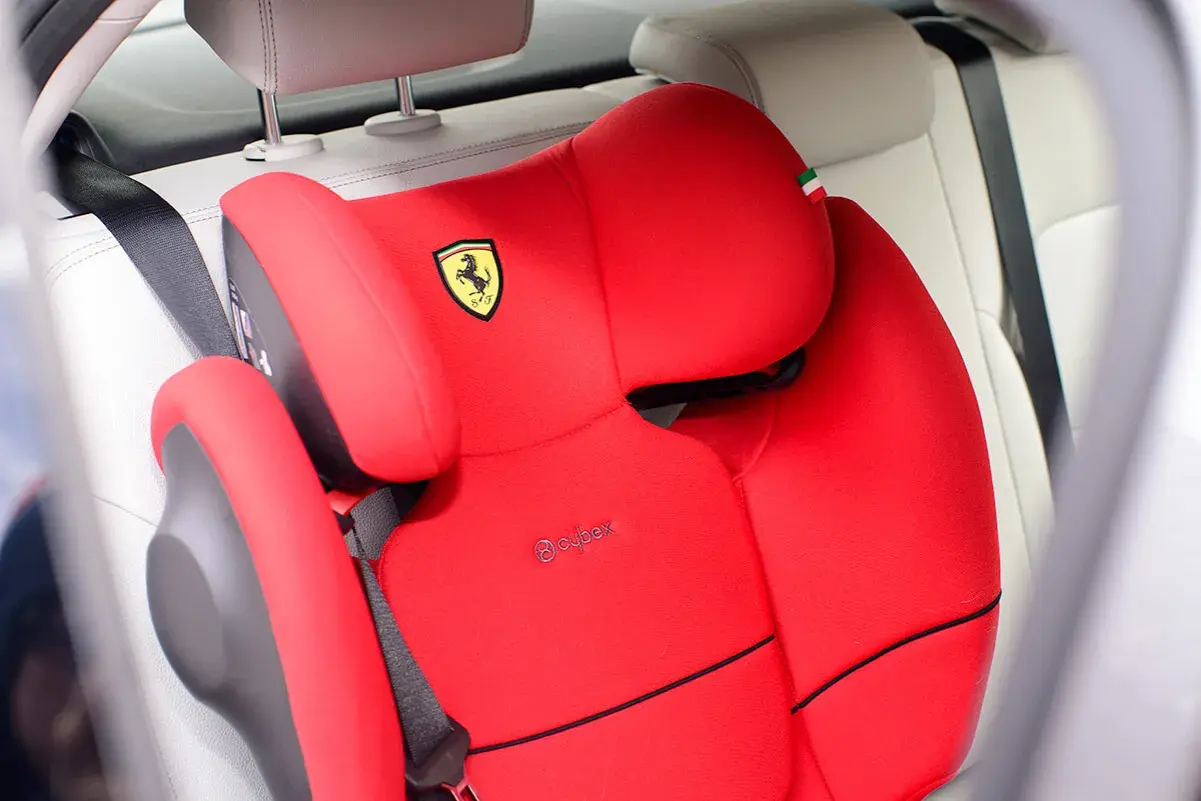 Czerwony fotelik samochodowy Cybex z logo Ferrari, zamontowany za pomocą pasa bezpieczeństwa. Instrukcja jak zamontować fotelik samochodowy.