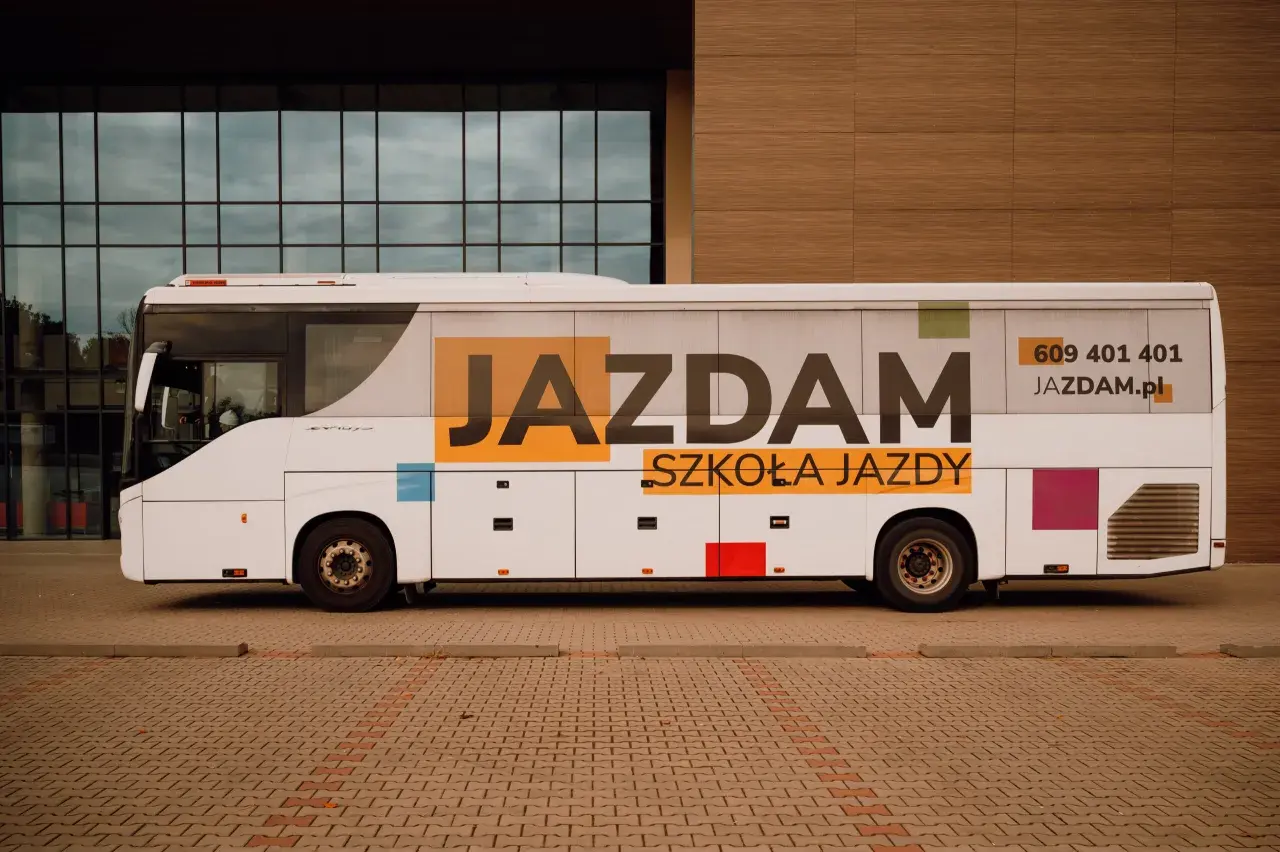 Biały autobus szkolny z napisem "JAZDAM SZKOŁA JAZDY" i numerem telefonu.