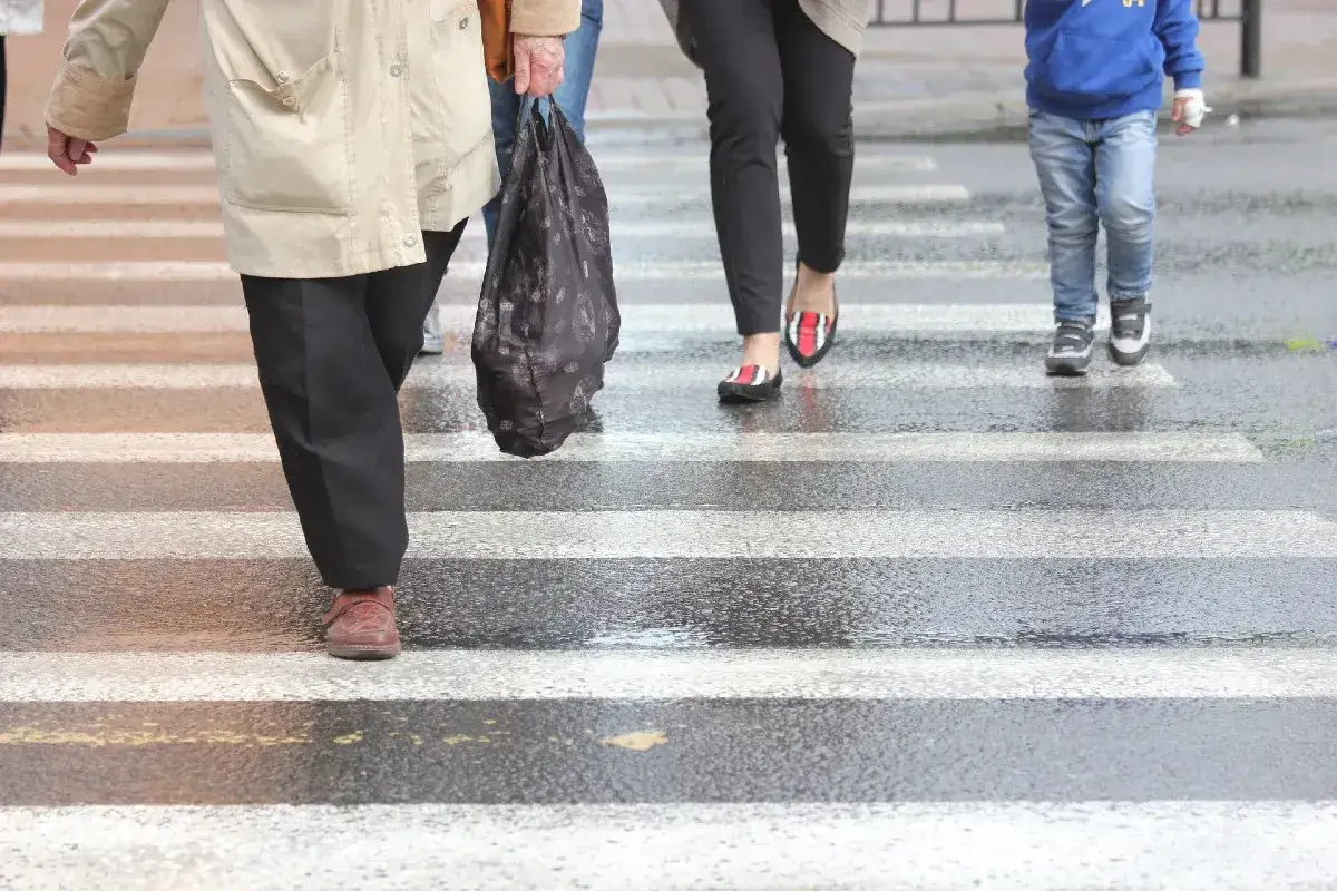 Ludzie przechodzą przez pasy, zgodnie z kodeksem drogowym. Dziecko w niebieskiej bluzie i dorośli na mokrym przejściu dla pieszych.
