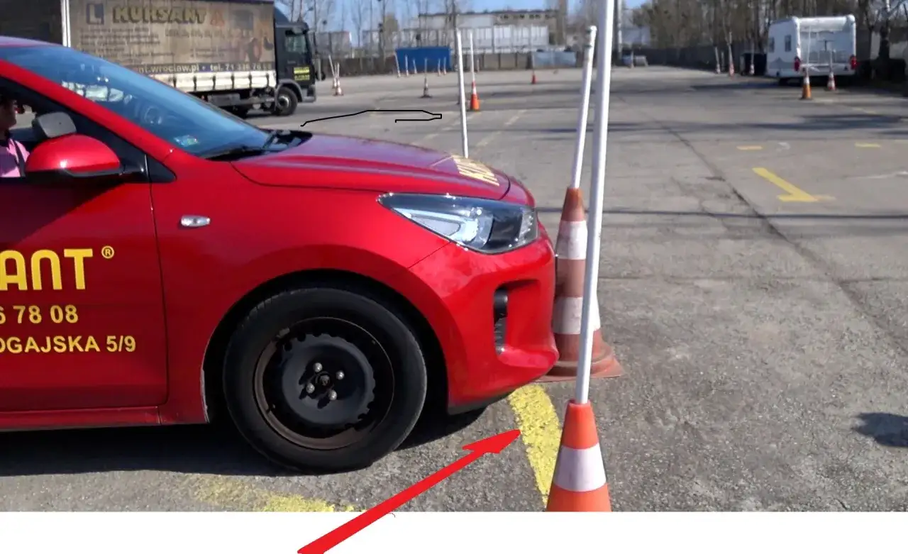 Czerwony samochód na placu manewrowym kat B, obok pachołków.