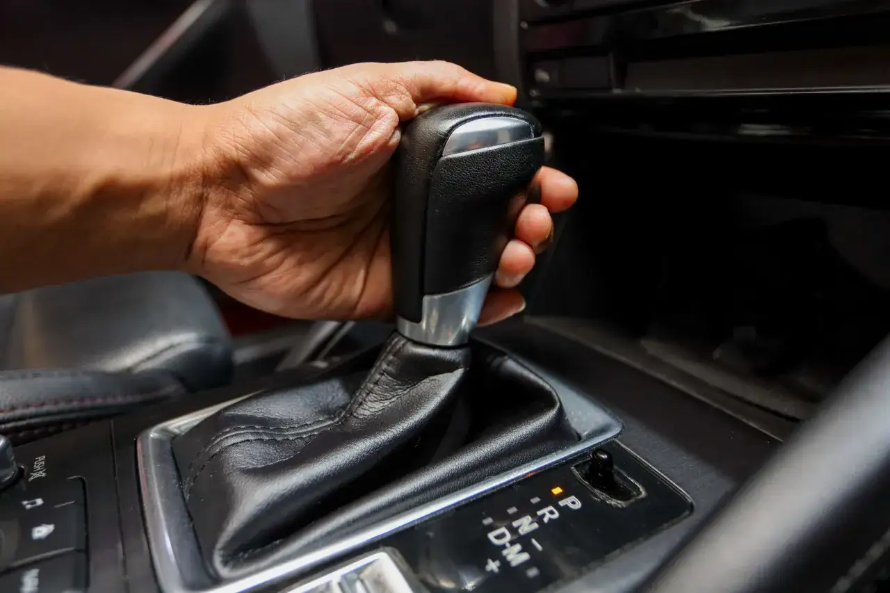 Dłoń na dźwigni zmiany biegów w samochodzie. Czy mając prawo jazdy na automat, można jeździć manualem? To pytanie nurtuje wielu kierowców.