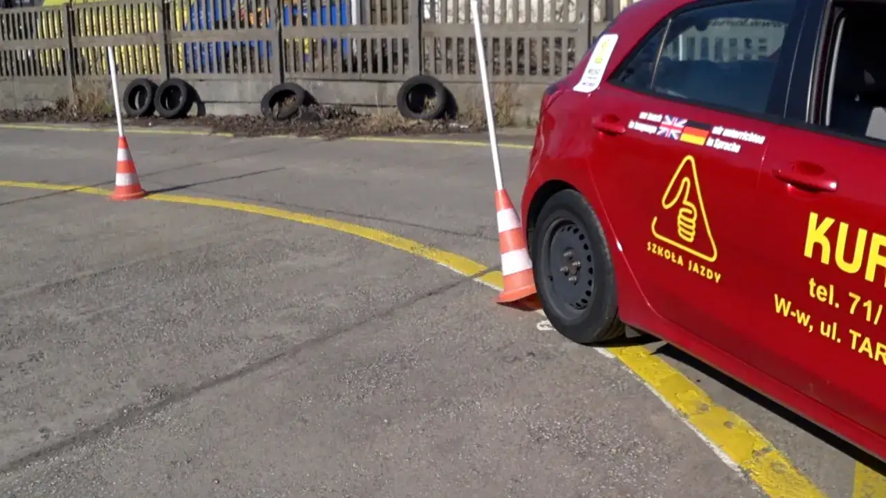 Czerwony samochód szkoleniowy na placu manewrowym kat B, obok pachołka.