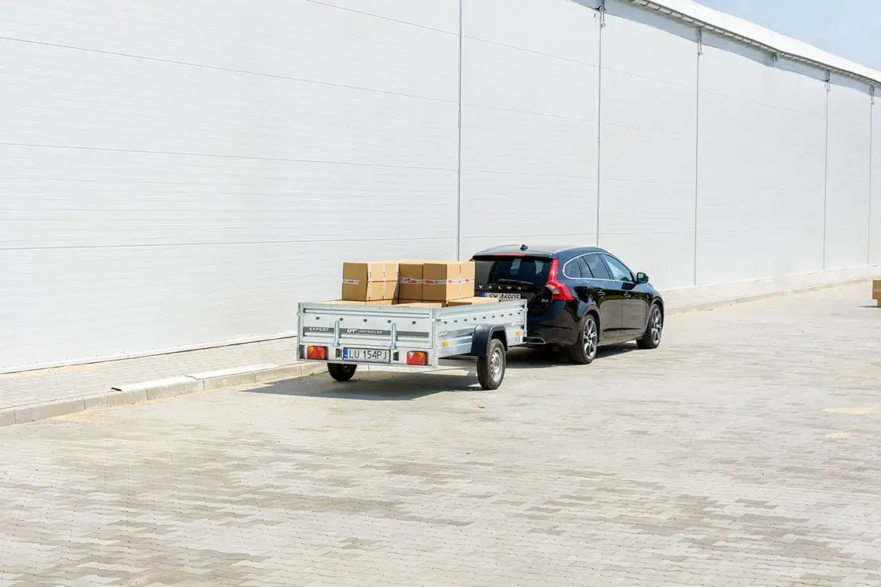 Czarna Volvo z przyczepą przewozi paczki. Dowiedz się, jak zarejestrować przyczepę rolniczą samoróbkę.