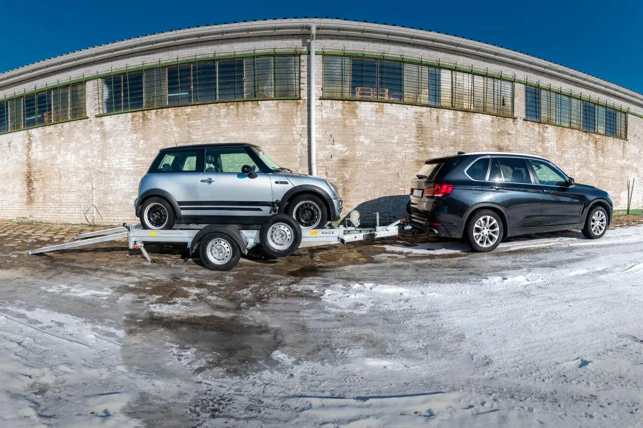 Mini Cooper na lawecie, obok BMW X5. Pokazano, jak zabezpieczyć auto na lawecie, by bezpiecznie dotarło do celu.