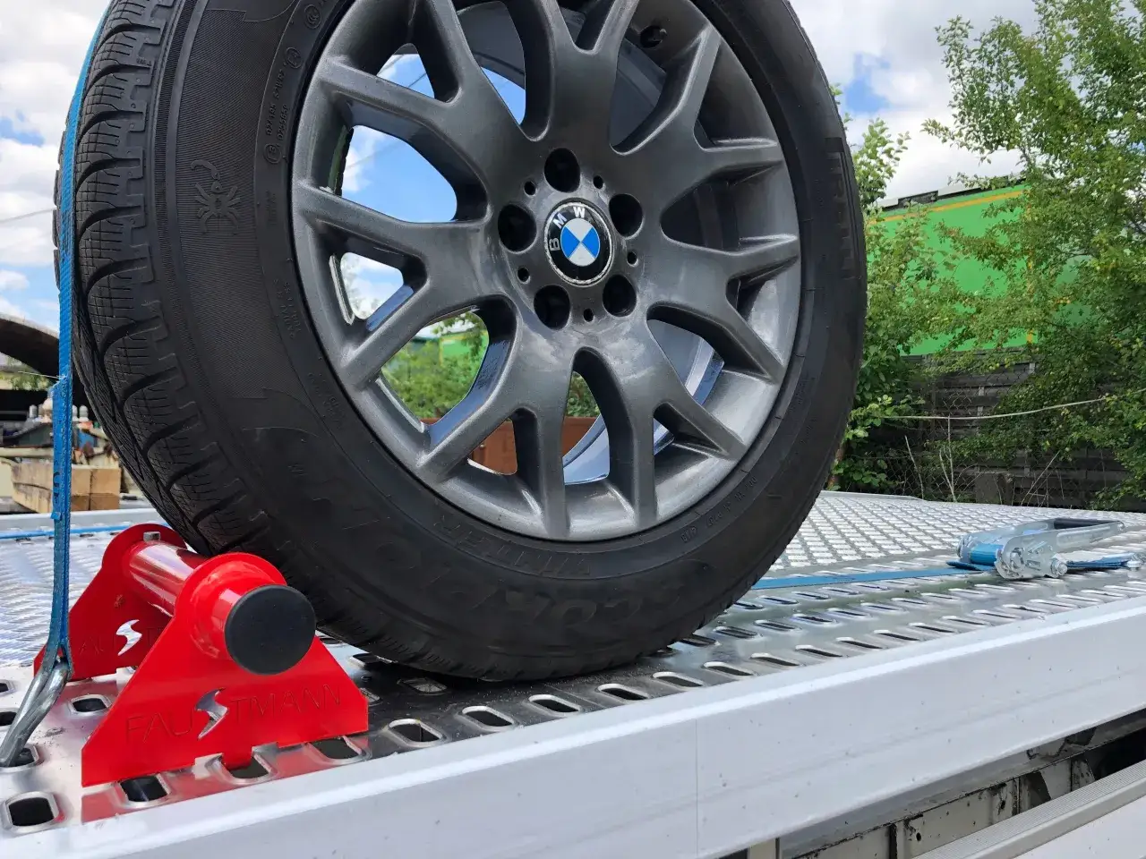 Czerwony klin pod koło BMW i pasy transportowe to klucz do tego, jak zabezpieczyć auto na lawecie. Bezpieczny transport gwarantowany.