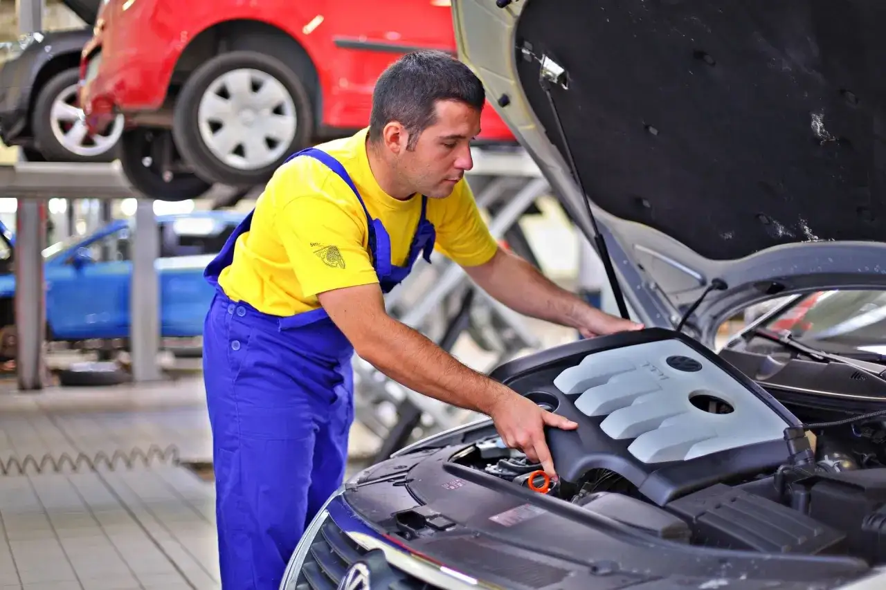 Mechanik w żółtej koszulce i niebieskich ogrodniczkach sprawdza silnik. Zastanawiasz się, ile zarabia mechanik samochodowy?