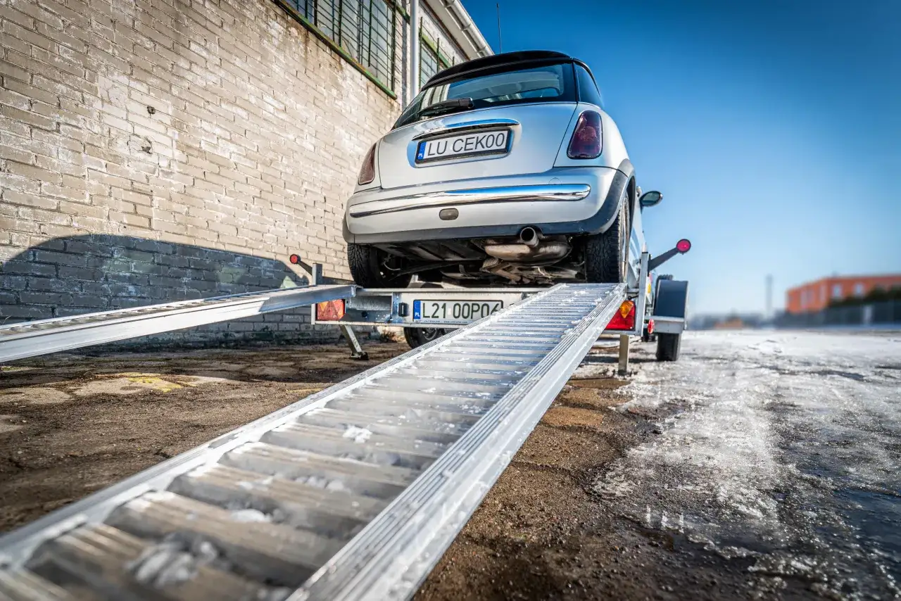 Srebrne Mini Cooper wjeżdża na lawetę, pokazując, jak zabezpieczyć auto na lawecie. Zimowy dzień, śnieg na ziemi.