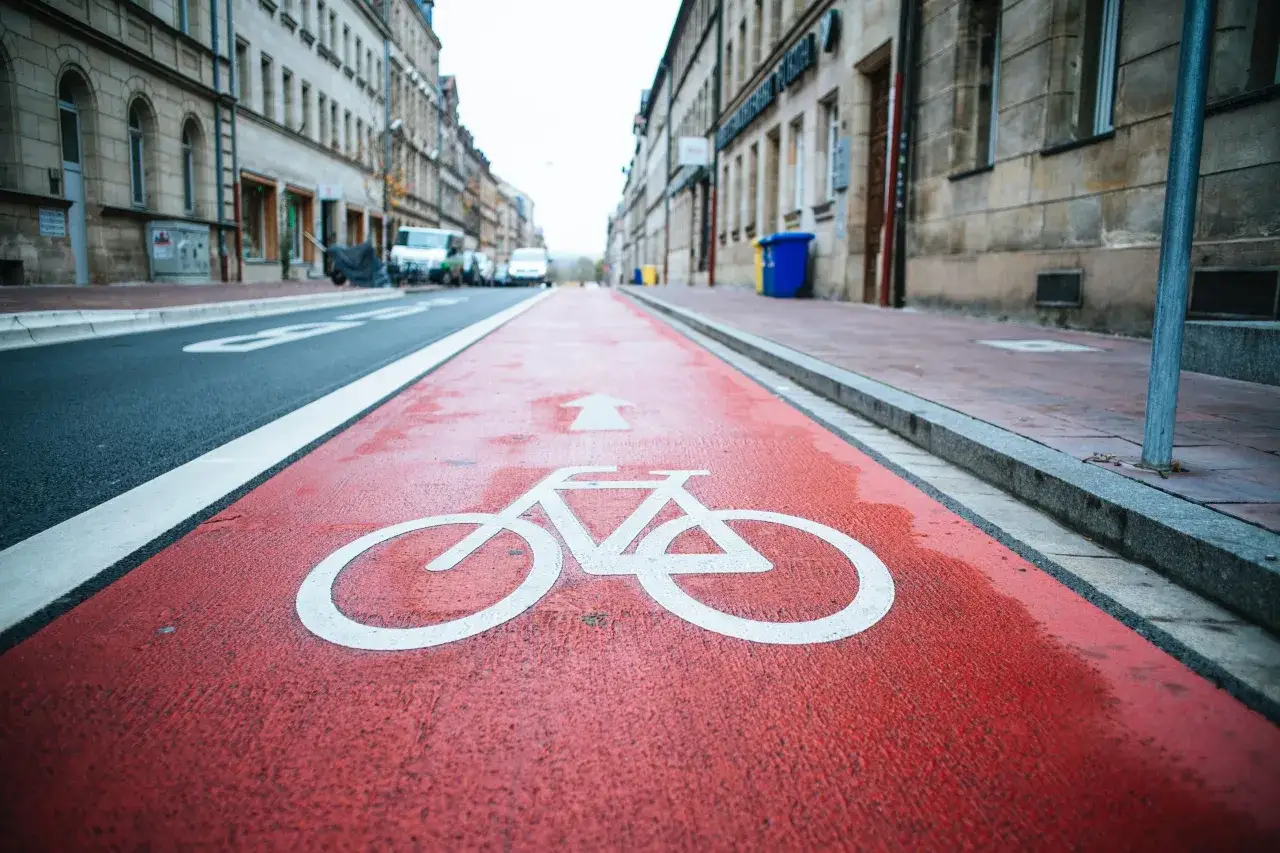Czerwony pas rowerowy z białym piktogramem roweru i strzałką. Pamiętaj, że masz obowiązek zachować bezpieczny odstęp od omijanego pojazdu.
