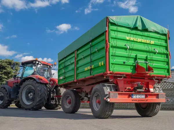 Czerwony traktor z zieloną przyczepą rolniczą. Zastanawiasz się, jak zarejestrować przyczepę rolniczą bez dokumentów? Sprawdź na www.pronar.pl.